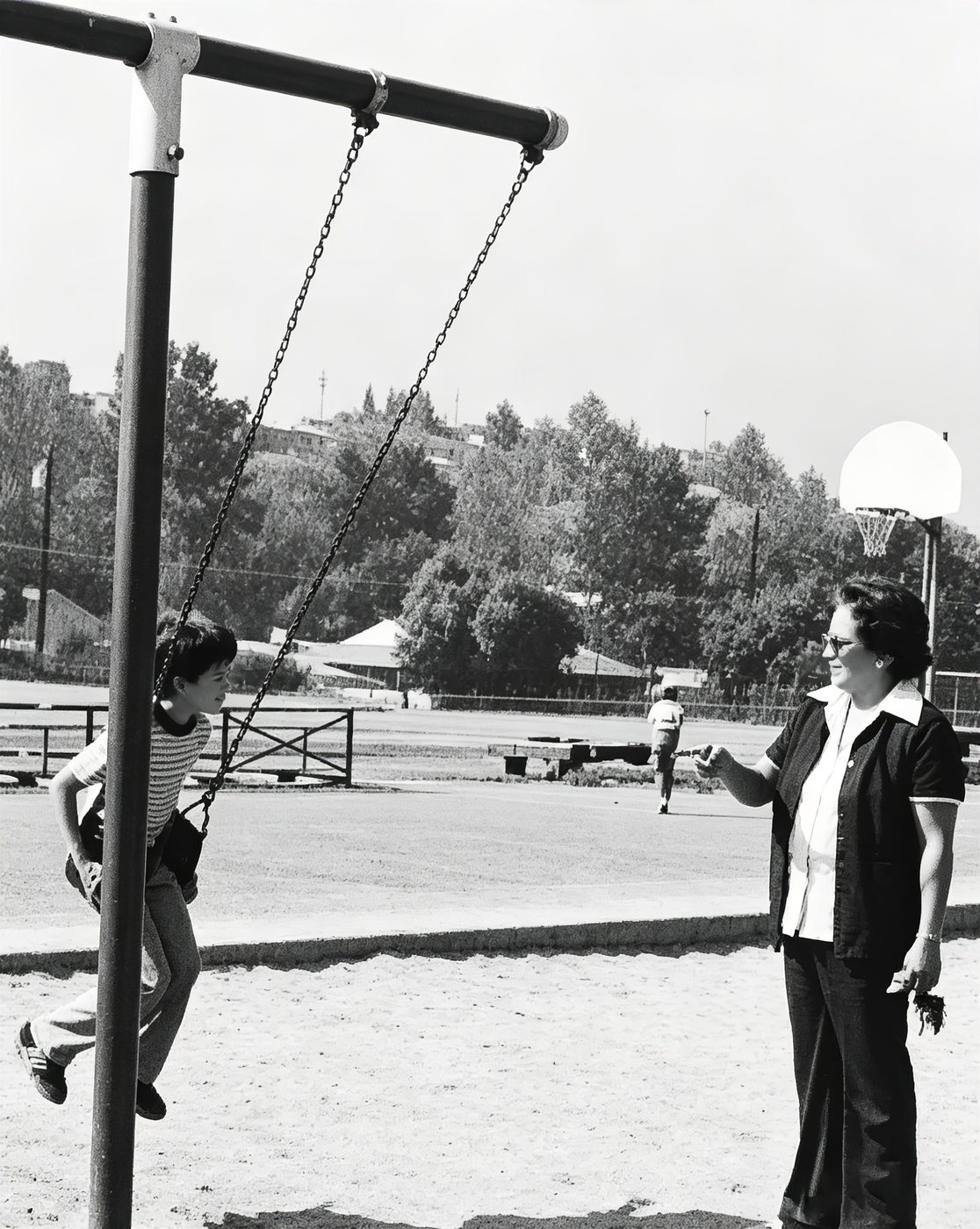 A child on the swings while a teacher watches