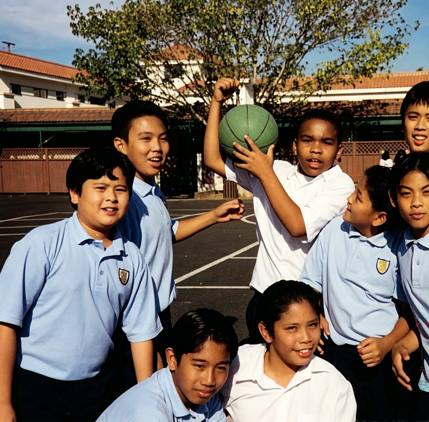 Students in crested polo uniforms play ball at recess